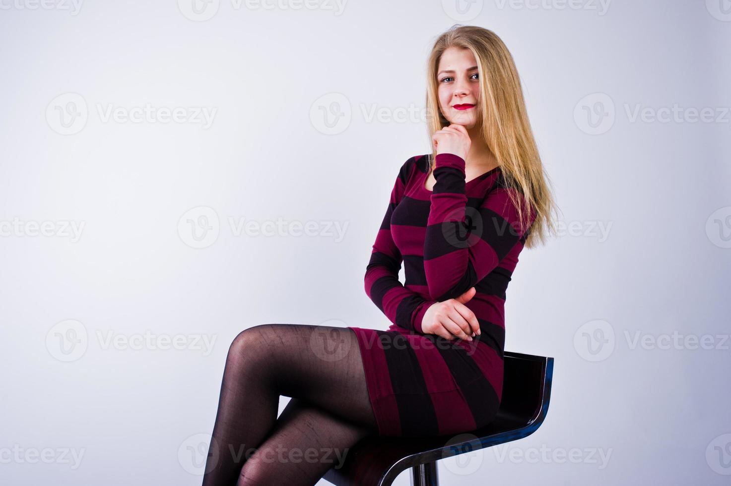 Portrait of a young woman in striped purple dress sitting on the chair in the studio. photo