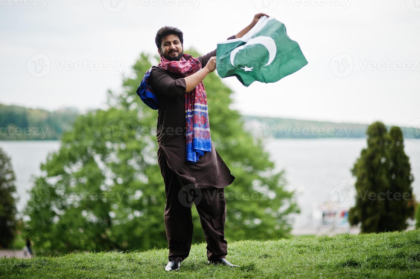 el hombre paquistaní usa ropa tradicional y sostiene la bandera de pakistán. foto