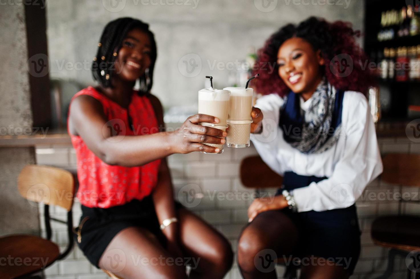 atractivas dos amigas afroamericanas sentadas en sillas contra el bar en el  pub y bebiendo café con leche. 10498344 Foto de stock en Vecteezy