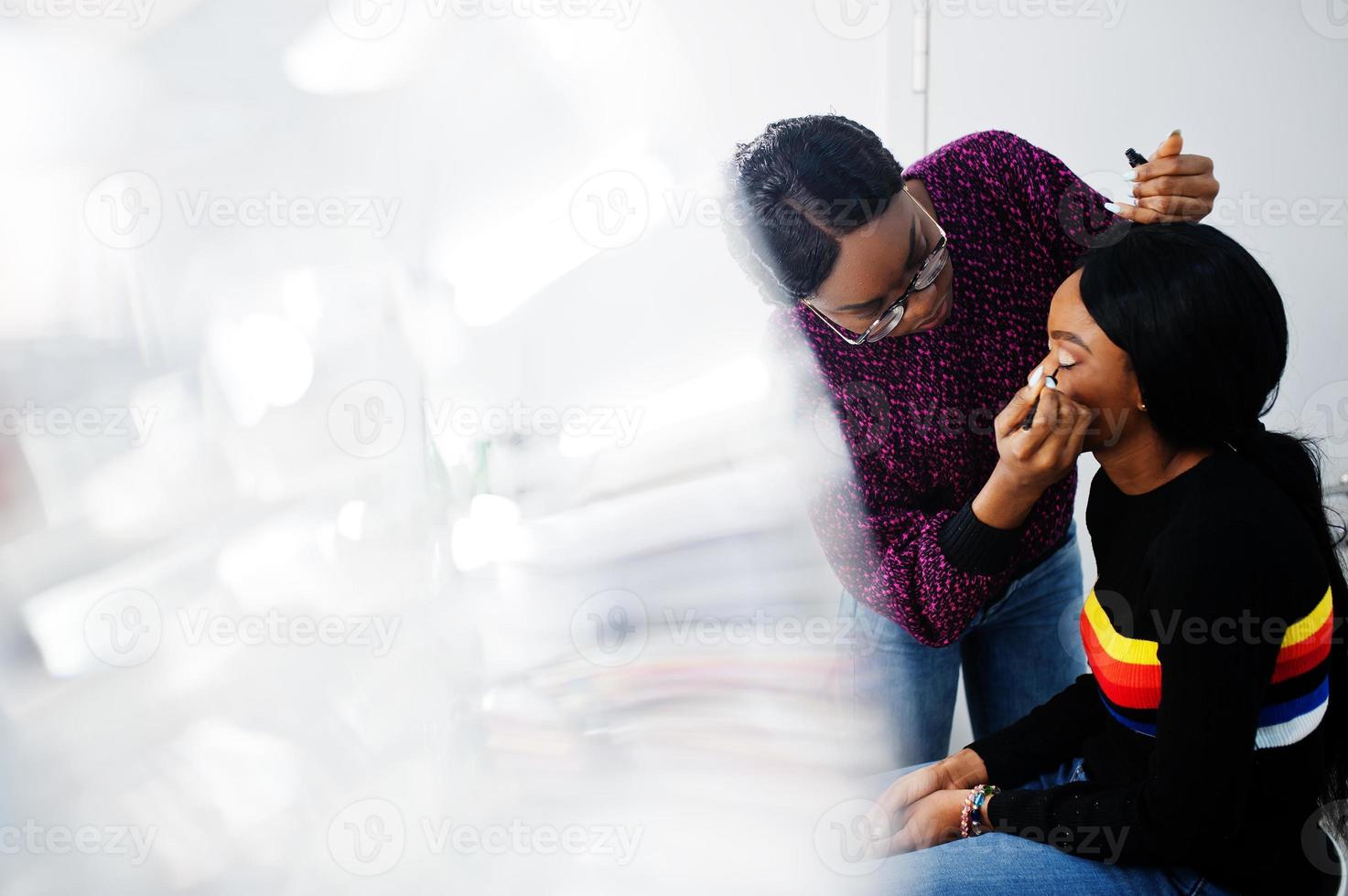 African American woman applying make-up by make-up artist at beauty saloon. photo