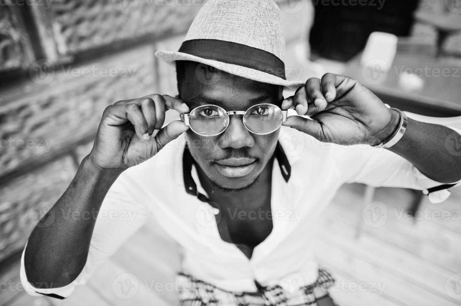 elegante hombre afroamericano con camisa blanca y pantalones de colores con sombrero y gafas al aire libre. chico modelo de moda negro. foto