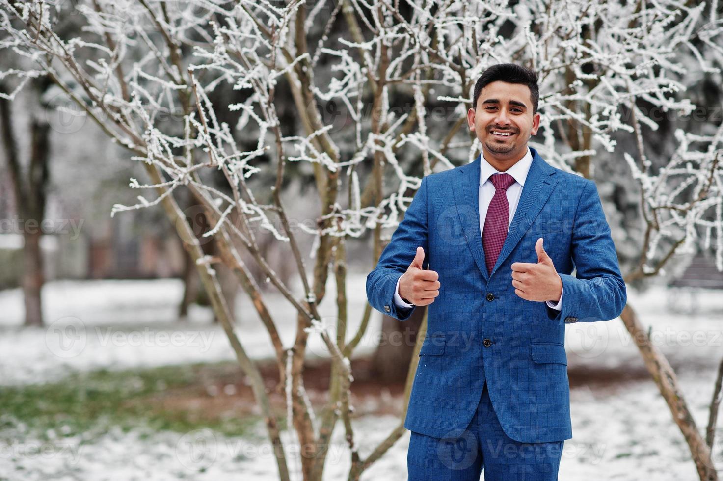 elegante modelo de hombre de moda indio en traje posado en el día de invierno muestra los pulgares hacia arriba. foto