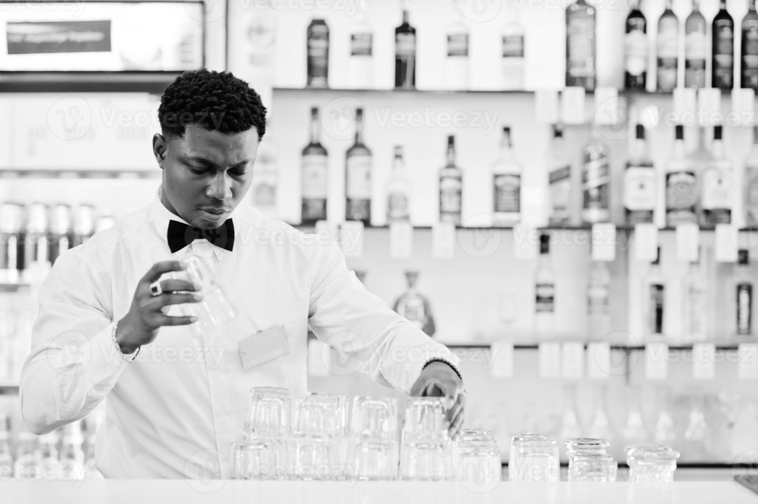 African american bartender wear on bow tie cleaning glasses at bar. photo