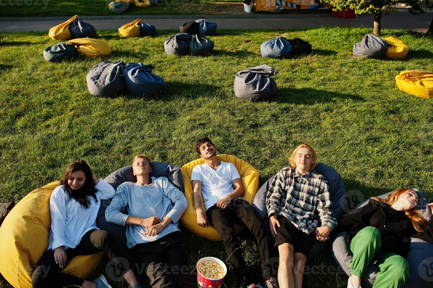 Young multi ethnic group of people watching movie at poof in open air cinema. photo