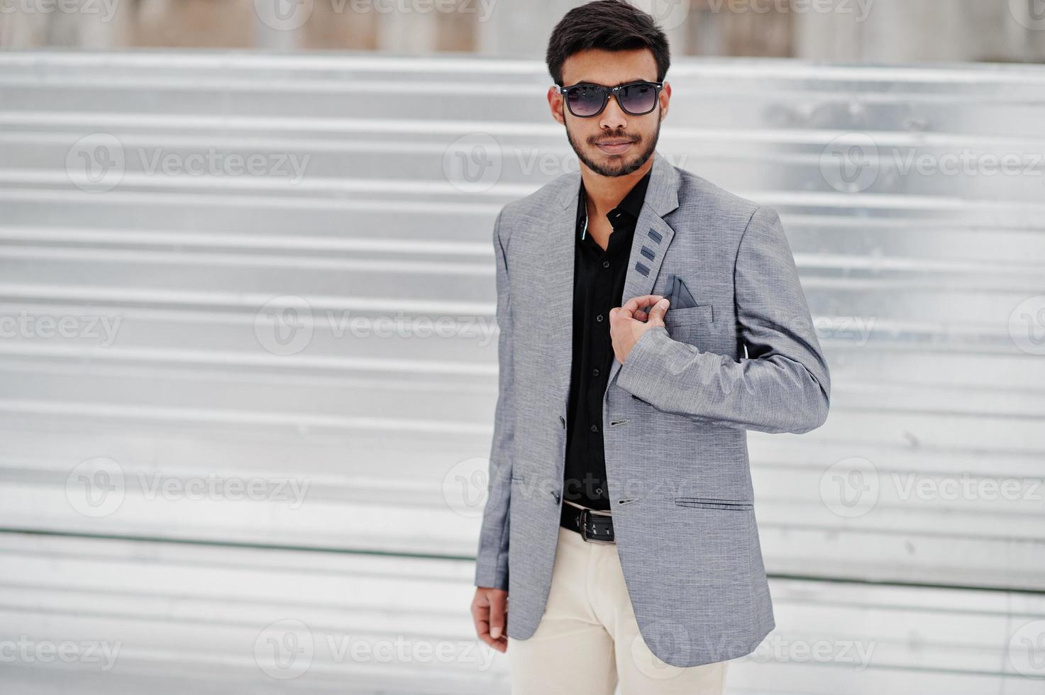 un joven indio informal con chaqueta plateada y gafas de sol posado sobre un fondo de acero. foto