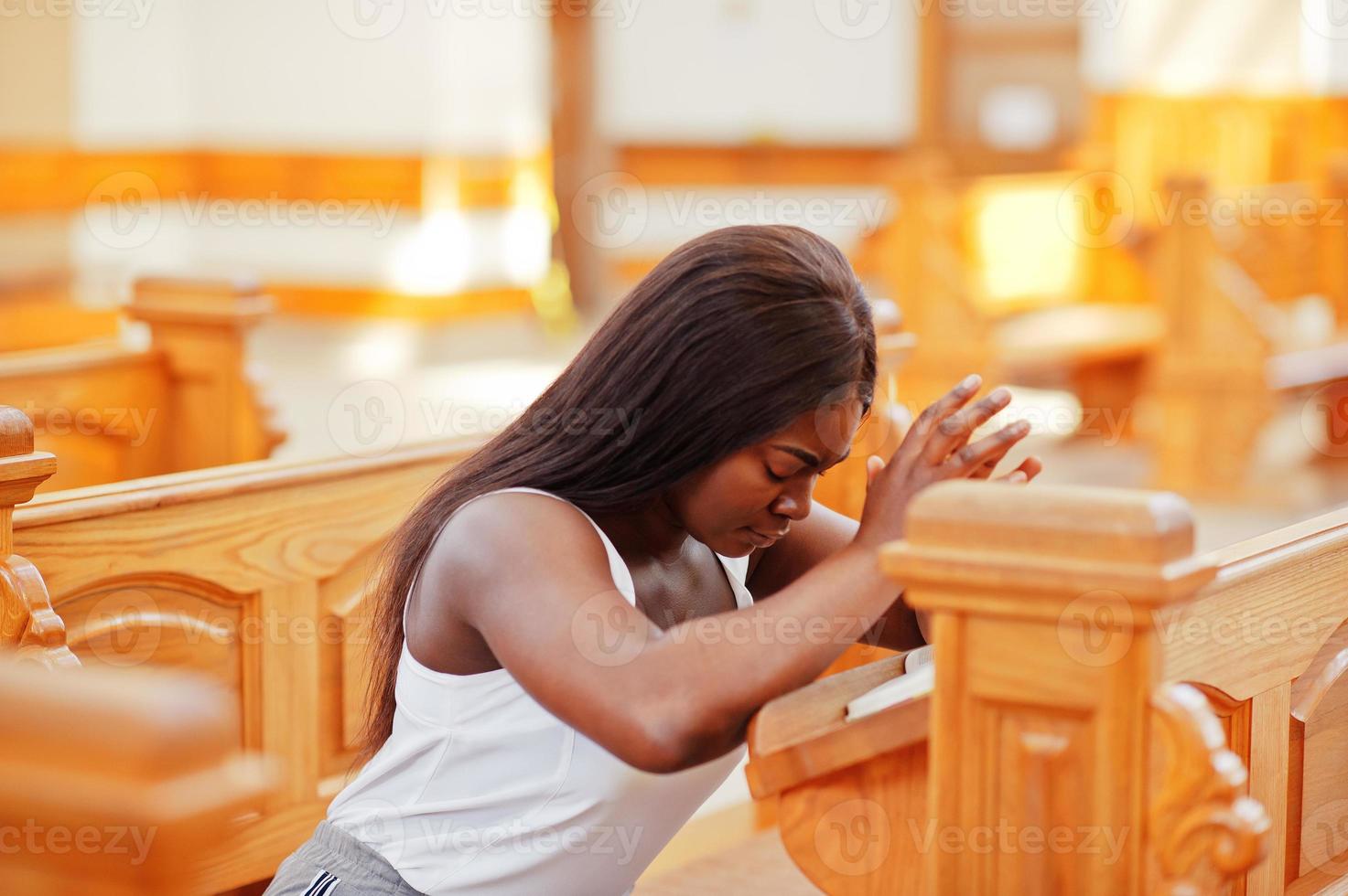 mujer afroamericana rezando en la iglesia. los creyentes meditan en la catedral y tiempo espiritual de oración. chica afro dobló las manos mientras se sentaba en el banco. foto