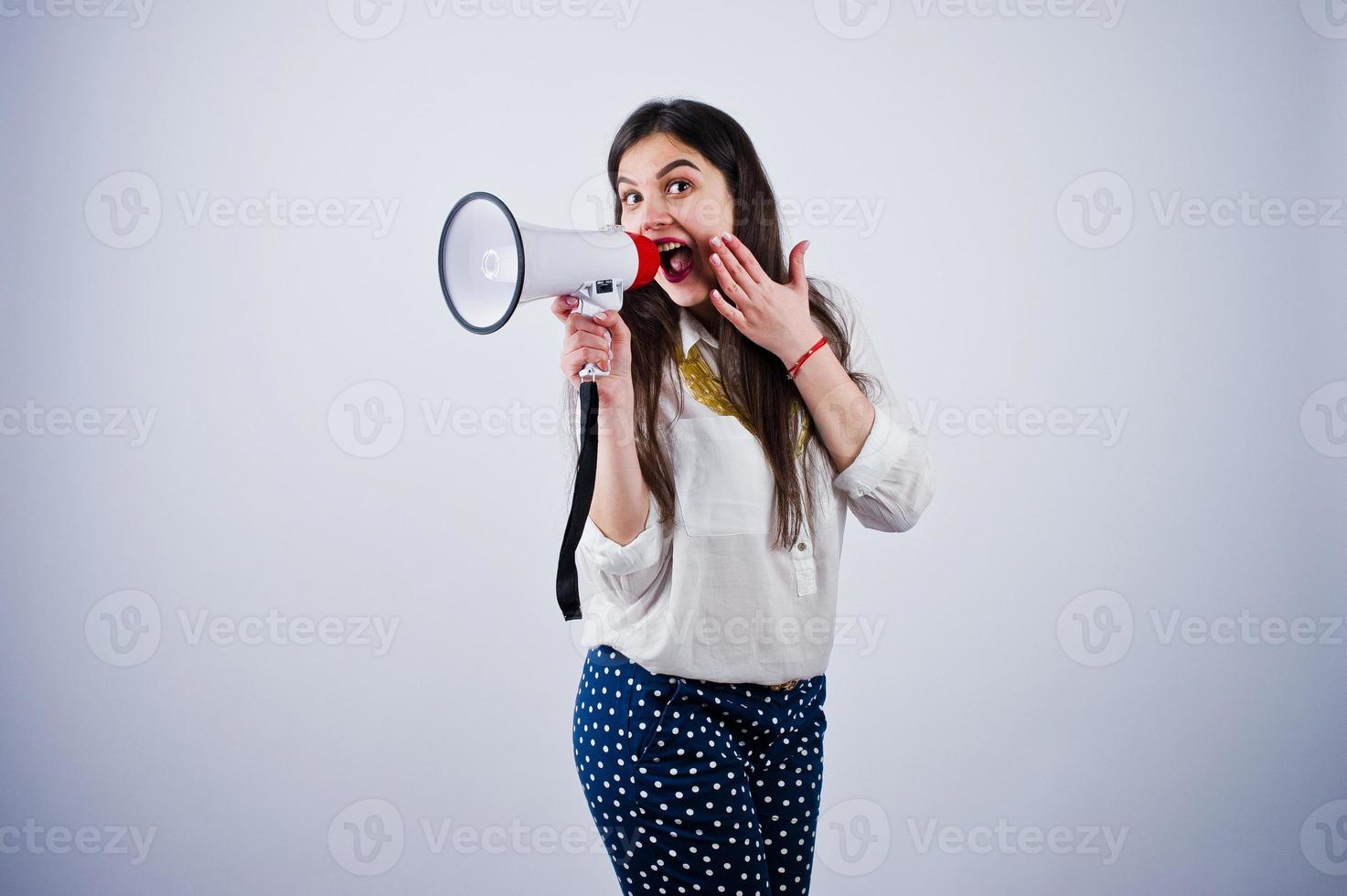 Portrait of a young woman in blue trousers and white blouse posing with megaphone in the studio. photo