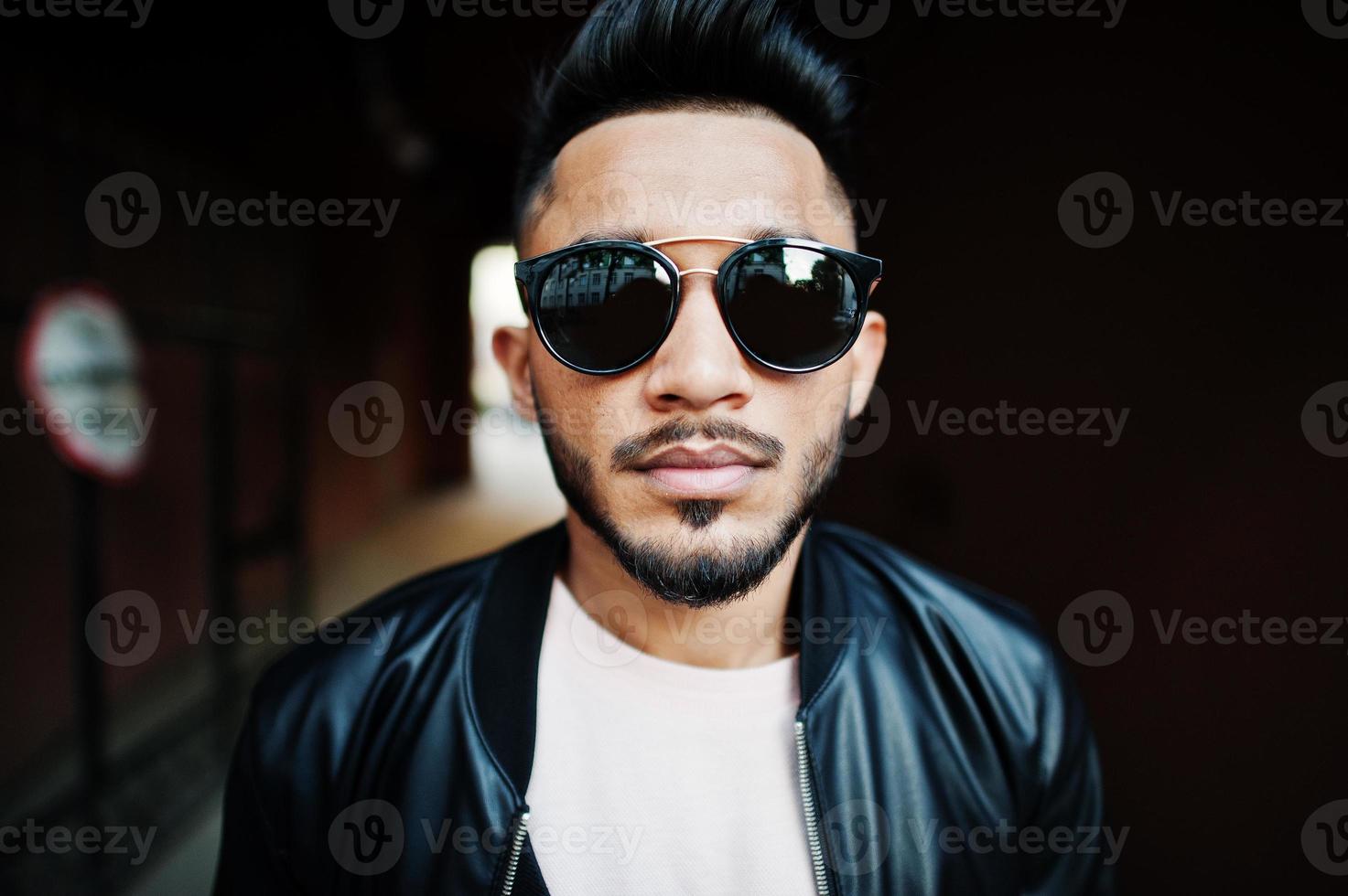 Stylish indian beard man at black leather jacket and sunglasses at tonnel arch. India model posed outdoor at streets of city. photo