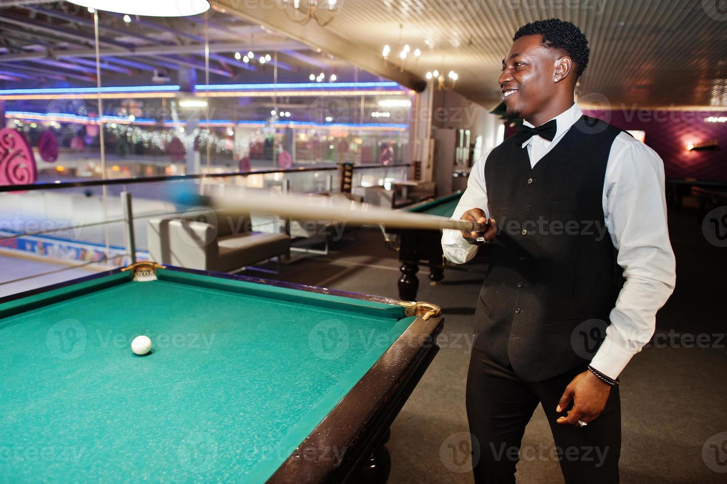 Young handsome african man wearing white shirt, black vest and bow tie play pool billiard. photo