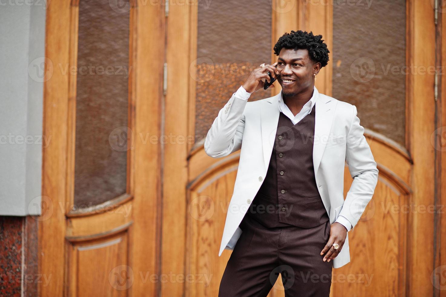 Thoughtful young handsome african american gentleman in formalwear. Black stylish model man in white jacket speak on phone. photo