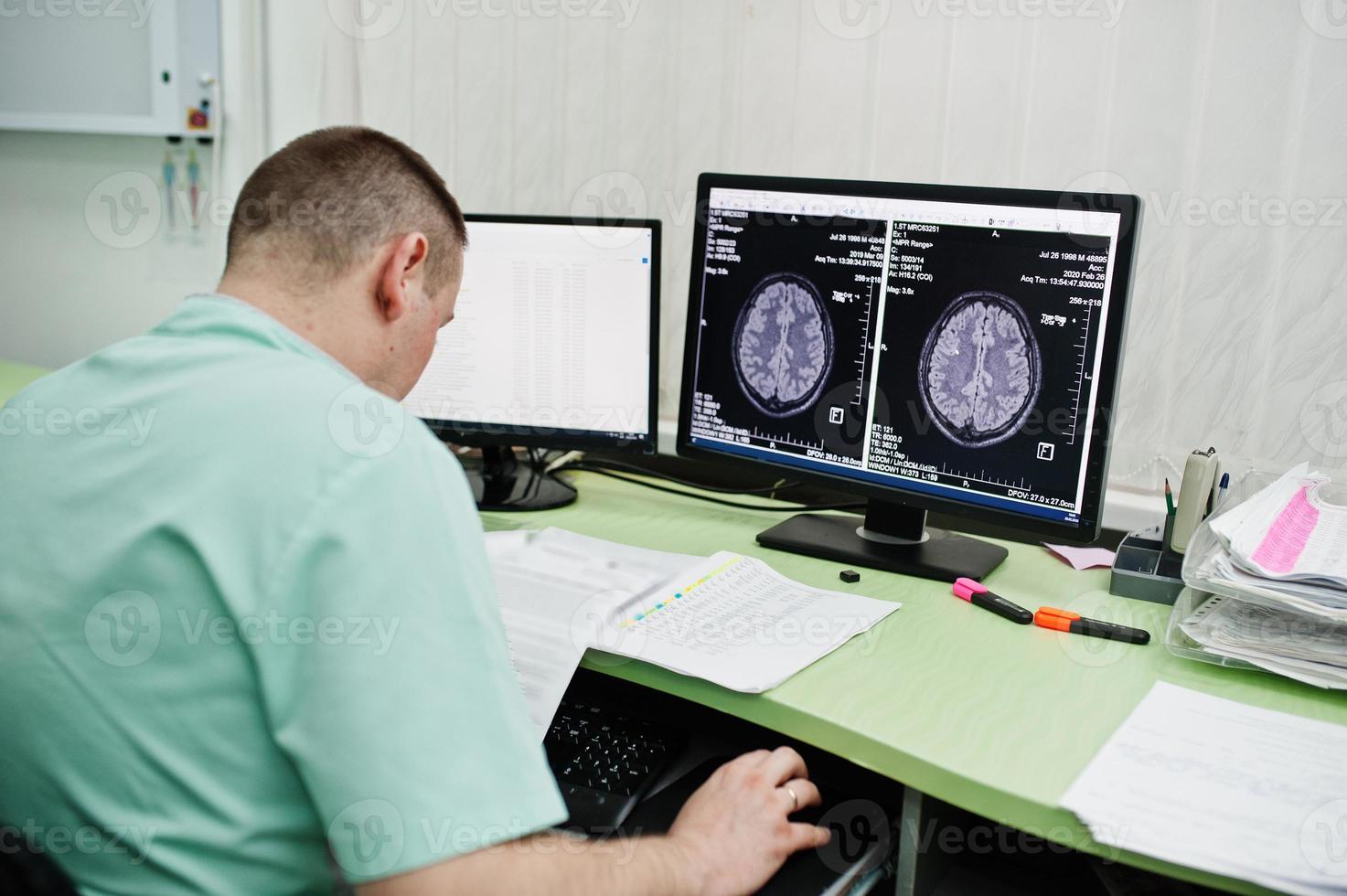 tema medico médico en la oficina de resonancia magnética en el centro de diagnóstico del hospital, sentado cerca de monitores de computadora con cerebro humano en él. foto