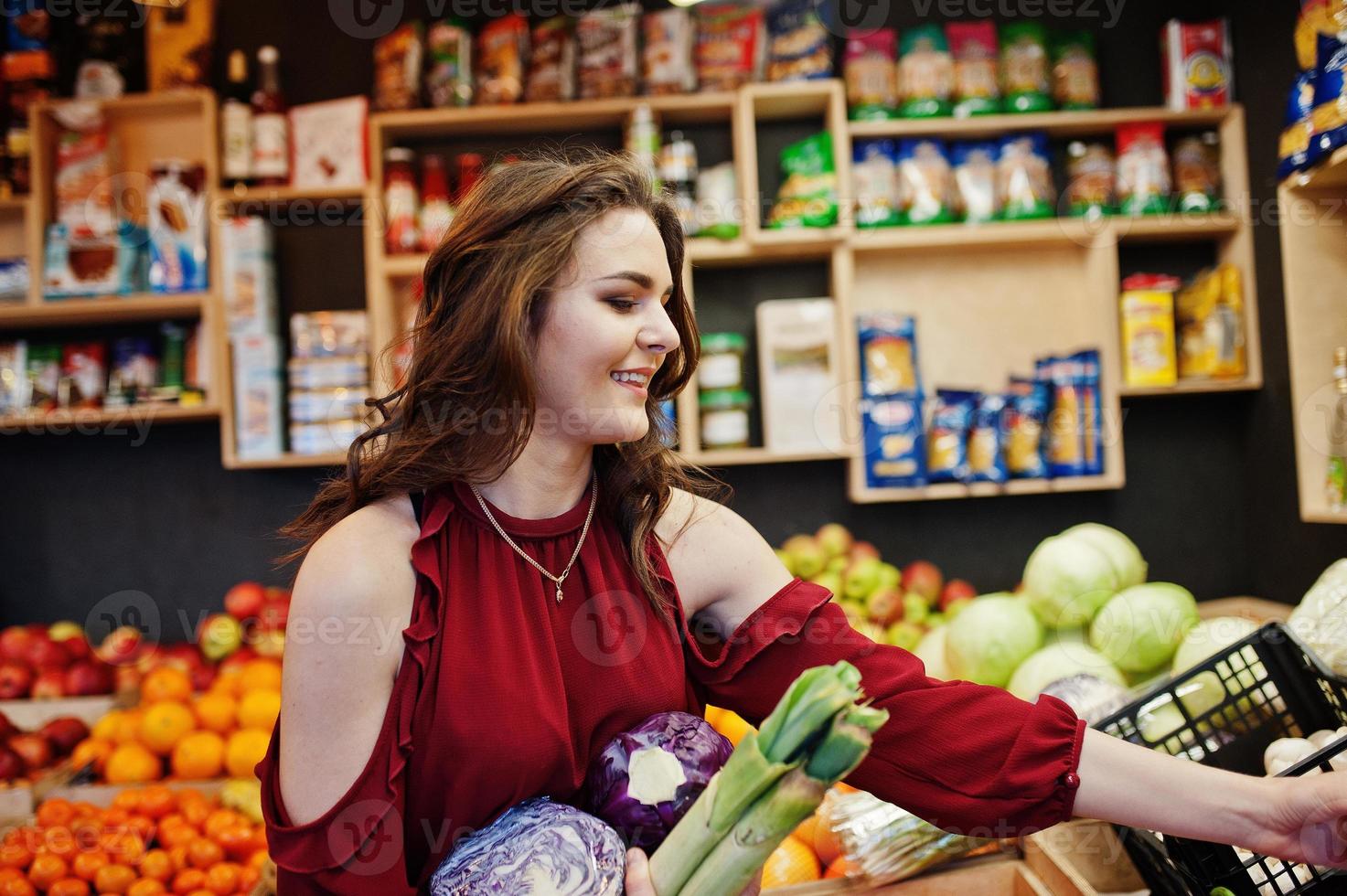 Girl in red holding different vegetables on fruits store. photo