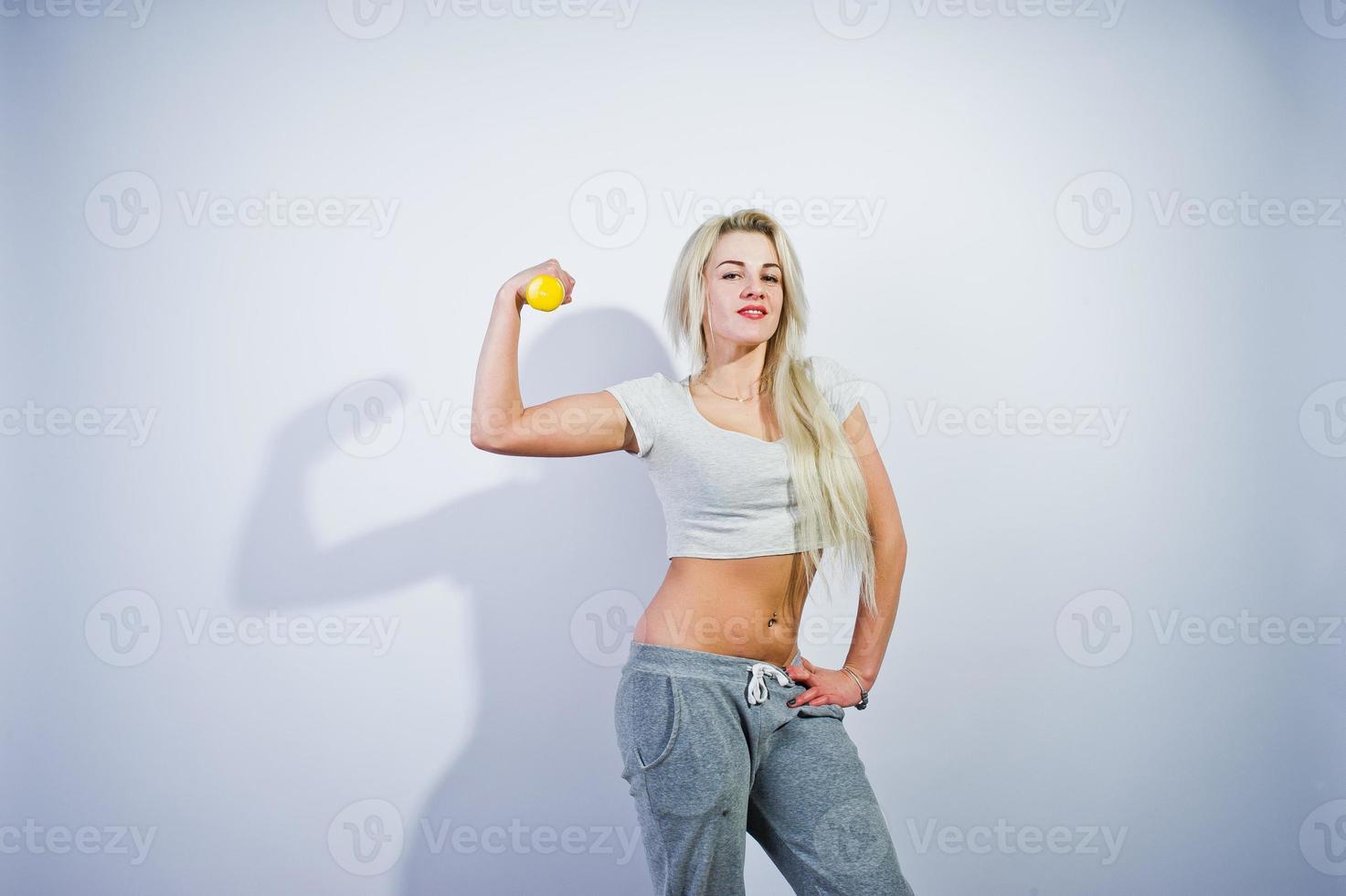 Blonde sporty girl with yellow dumbbell posed at studio against white background. photo