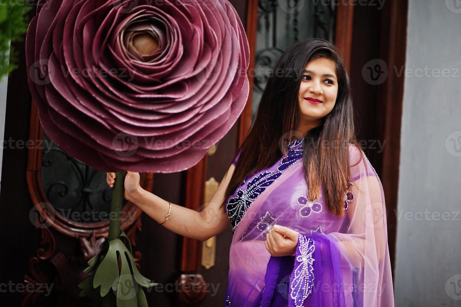 Indian hindu girl at traditional violet saree posed at street near big decorated rose. photo