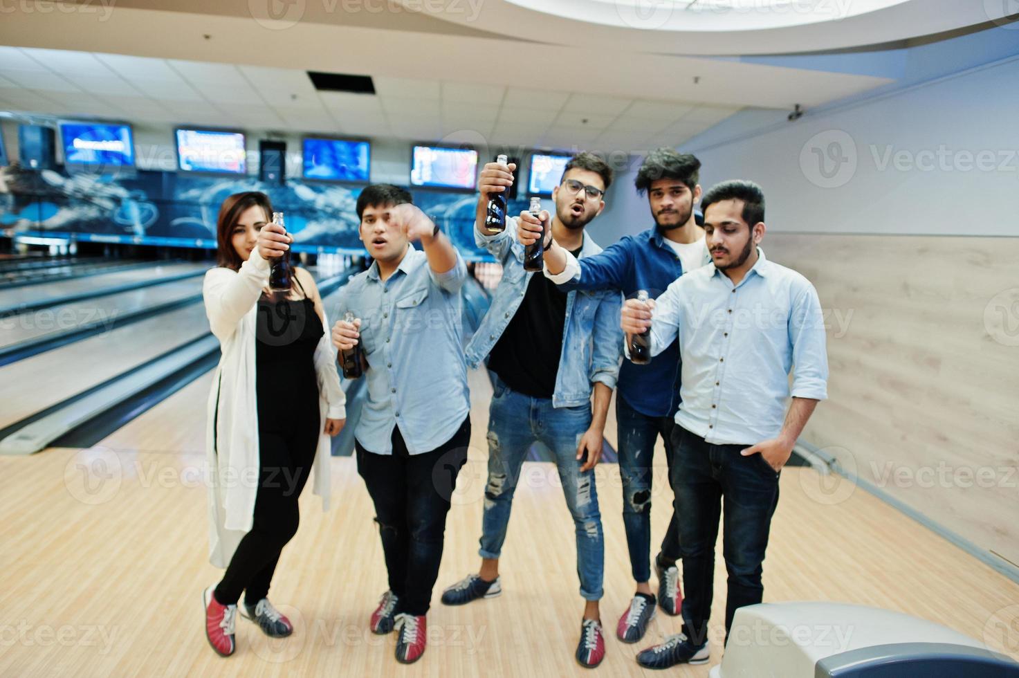 Group of five south asian peoples having rest and fun at bowling club. Holding cold soda drinks from glass bottles. photo