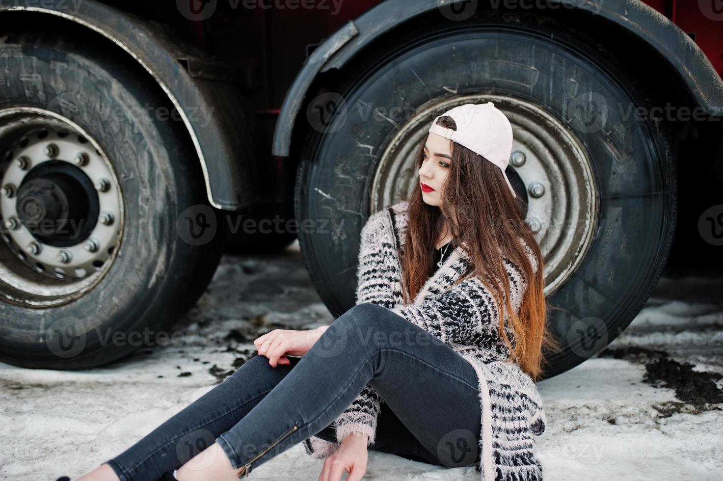 Brunette stylish casual girl in cap sitting against truck wheels. photo