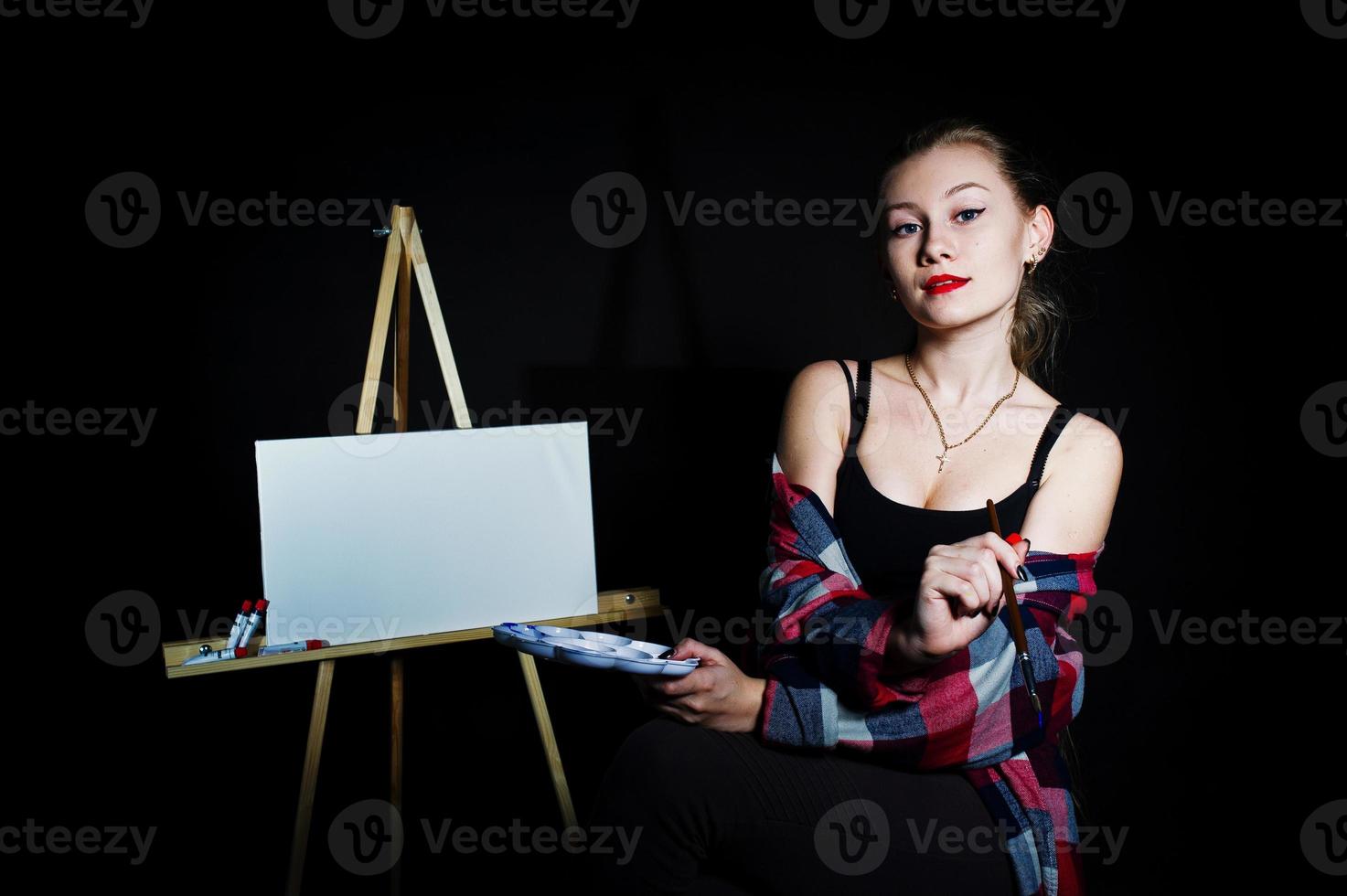 Beautiful woman artist painter with brushes and oil canvas posing in studio isolated on black. photo