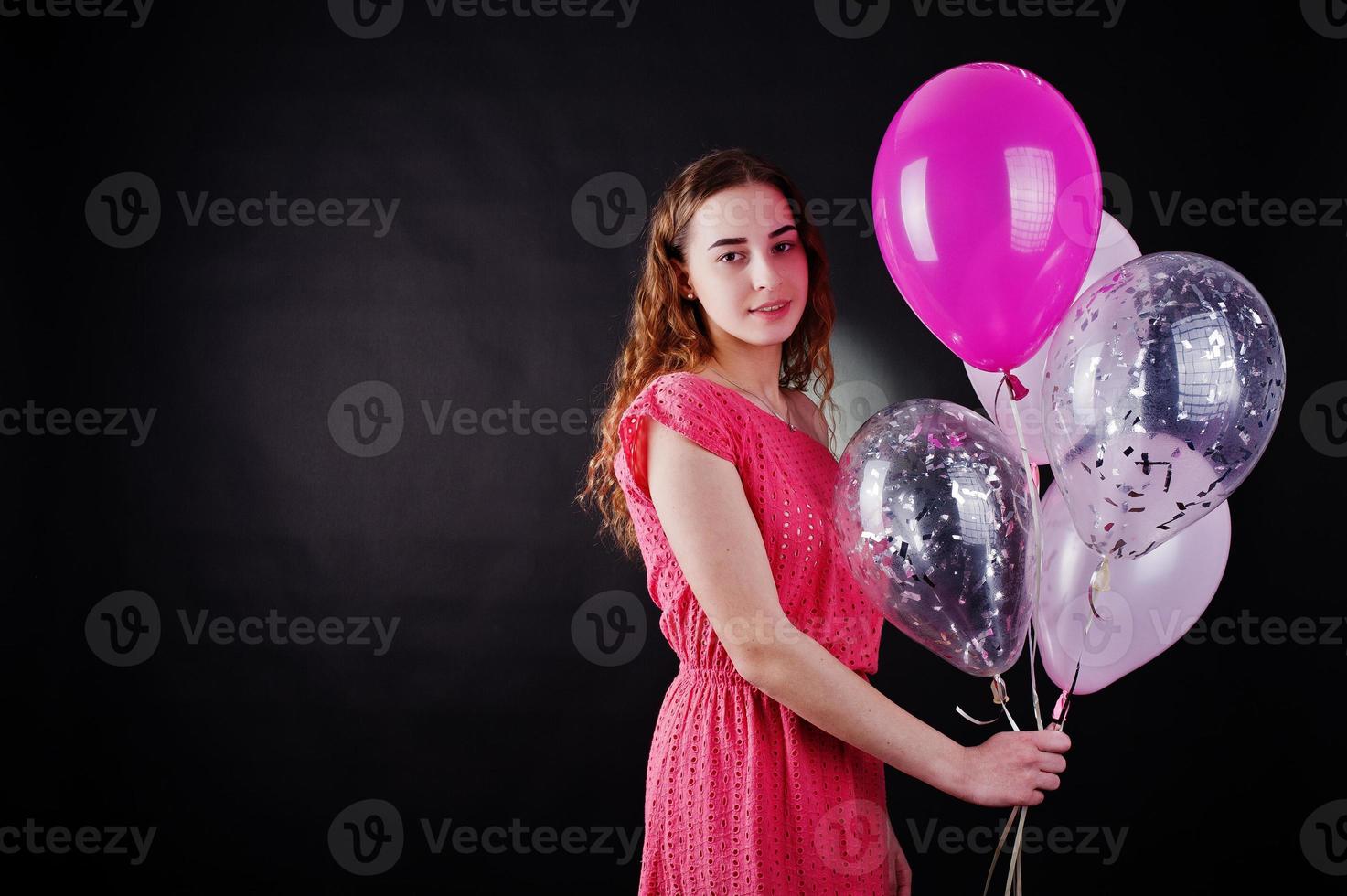 Young girl in red dress with balloons against black background on studio. photo