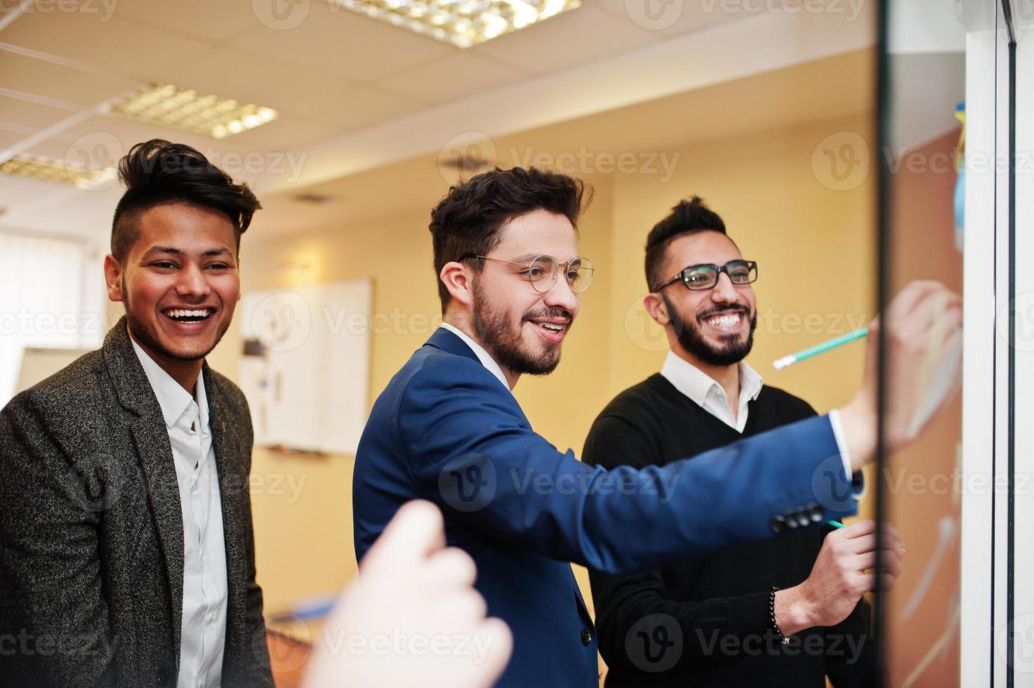 hombre de negocios apuntando sobre vidrio con notas de papel de colores. grupo diverso de empleados varones en ropa formal usando pegatinas. foto