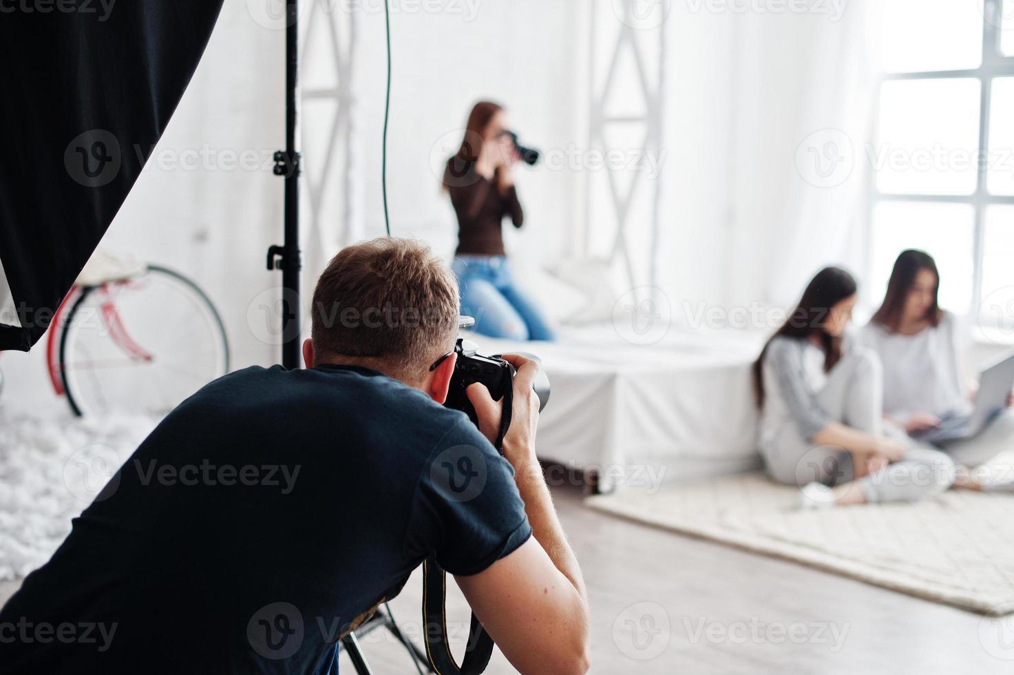 The team of two photographers shooting twins models girls on studio who are looking at laptop. Professional photographer on work. photo