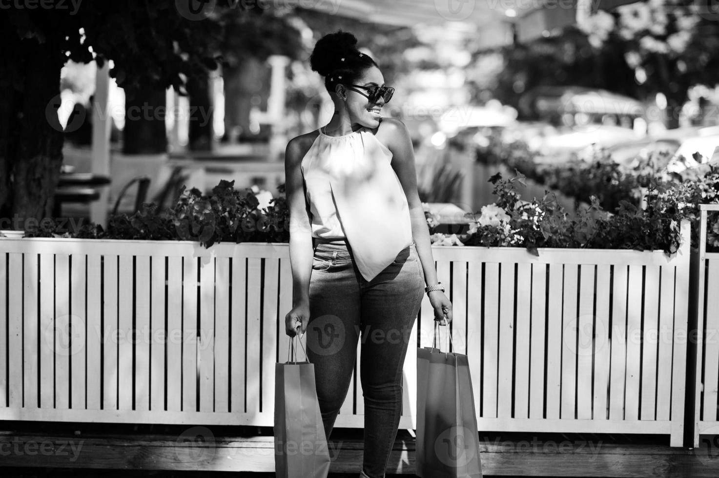 Casual african american girl with colored shopping bags walking outdoor. Stylish black woman shopping. photo