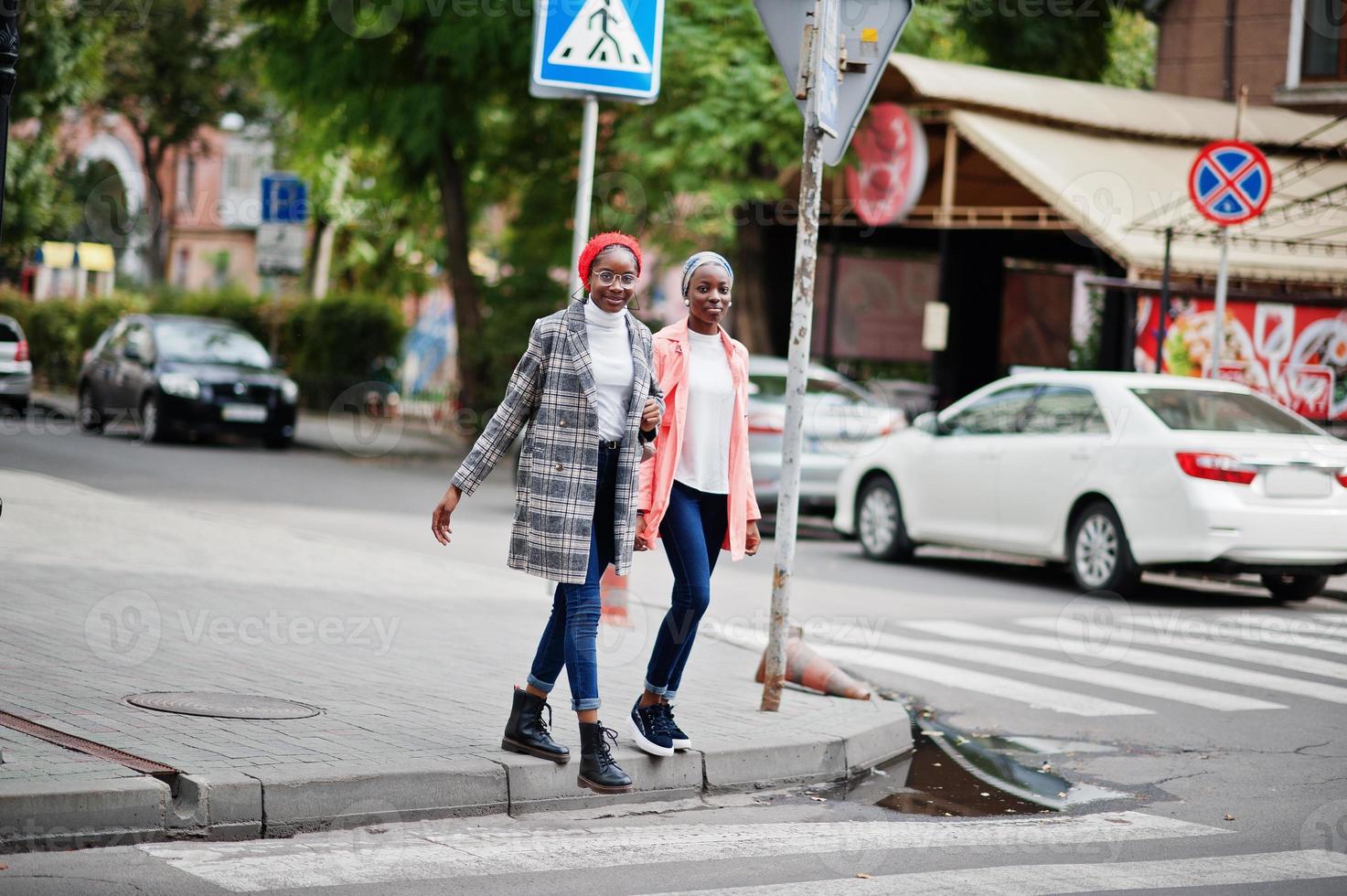 dos jóvenes mujeres musulmanas africanas modernas, atractivas, altas y delgadas con hiyab o turbante en la cabeza y abrigo caminando sobre peatones cruzados. foto