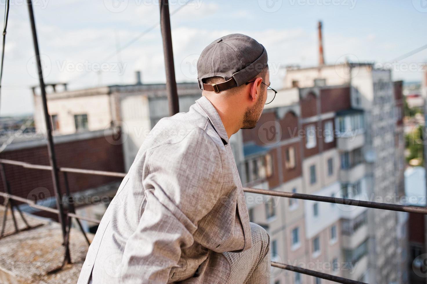 Dreamer stylish macho man in gray suit, hat and glasses posed on the roof. photo