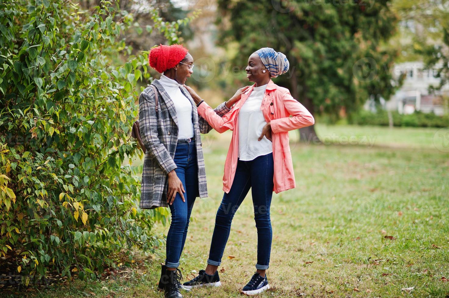 Two young modern fashionable, attractive, tall and slim african muslim womans in hijab or turban head scarf and coat posed at park together. photo