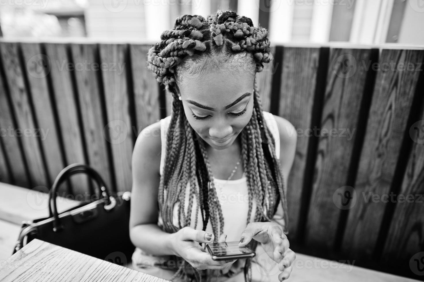 chica afroamericana de moda con pantalones rosas y rastas rojas posadas al aire libre con teléfono móvil. foto