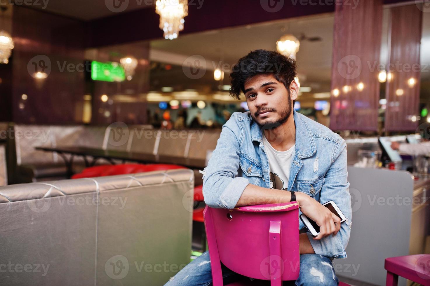 Stylish asian man wear on jeans jacket sitting on chair against bar in club. photo