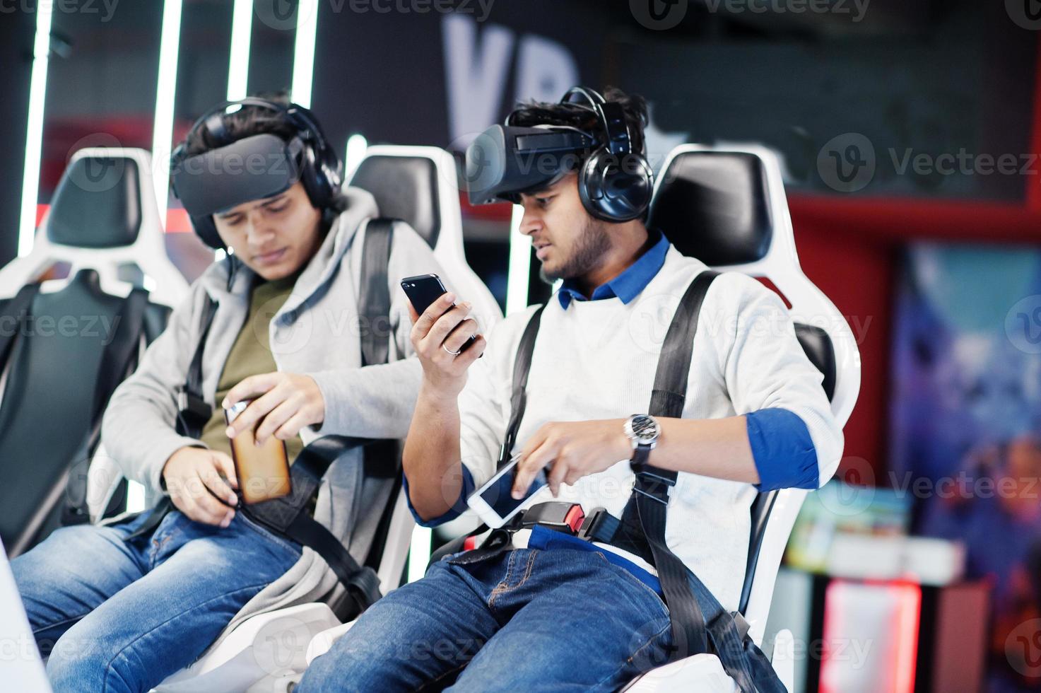 Two young indian people having fun with a new technology of a vr headset at virtual reality simulator with mobile phone at hands. photo
