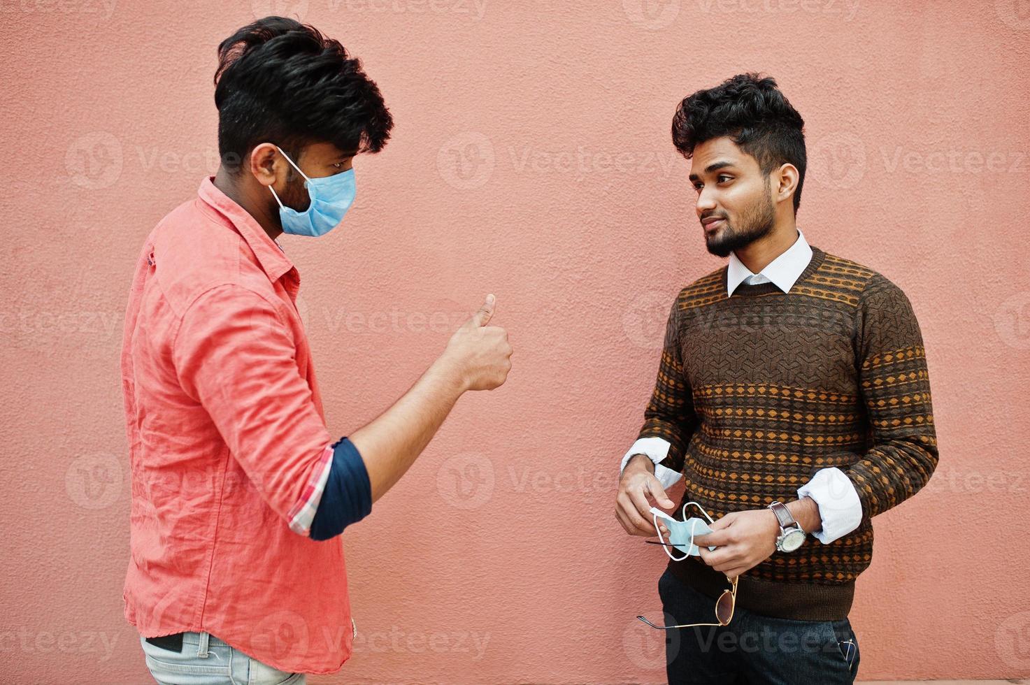 Coronavirus covid-19 concept. Two south asian indian man wearing mask for protect from corona virus isolated on pink background. Social distance. photo