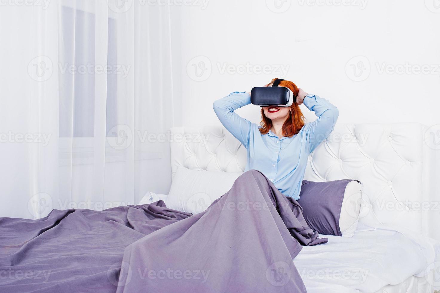 Red haired girl in bed with vr glasses at studio room. photo