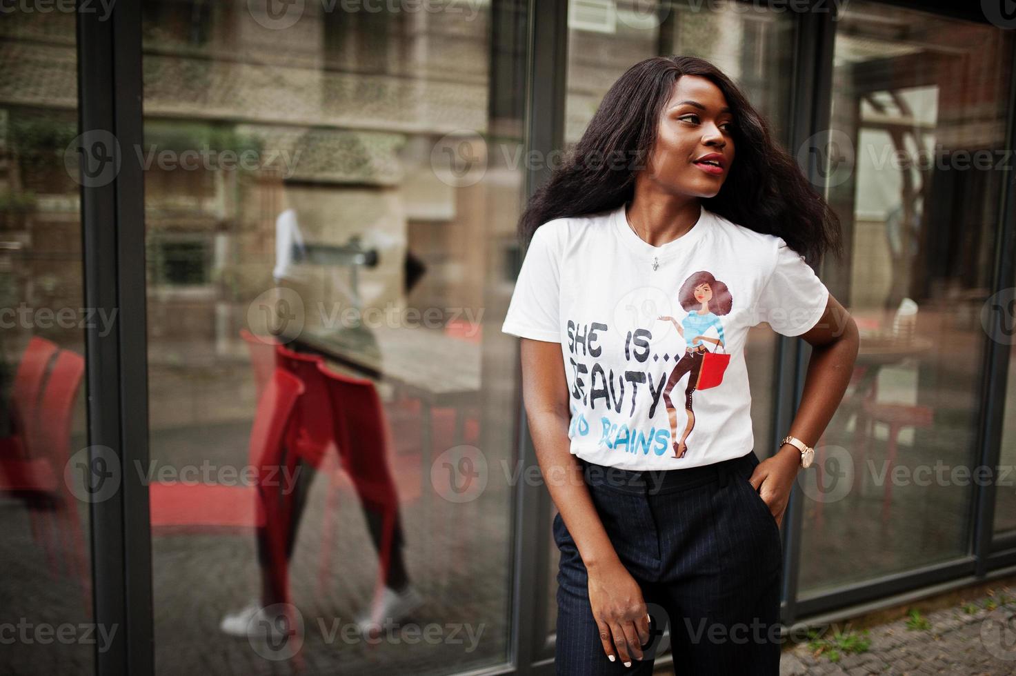 Stylish african american woman in printed t-shirt posed outdoor against window. photo