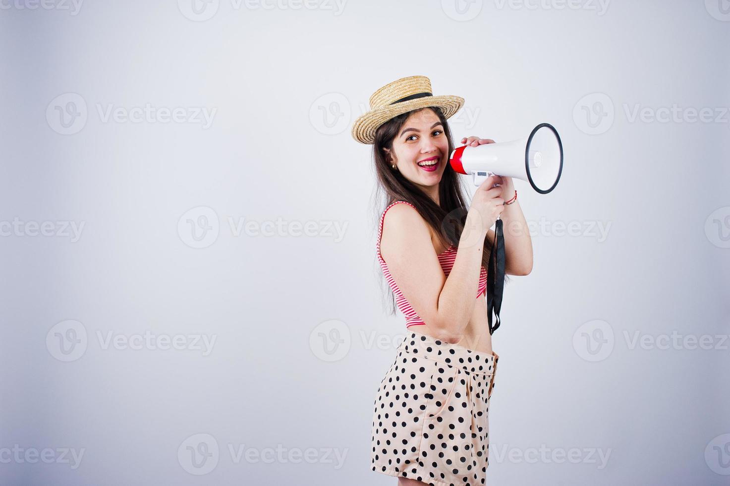 retrato de una hermosa joven en traje de baño y sombrero habla por megáfono en el estudio. foto