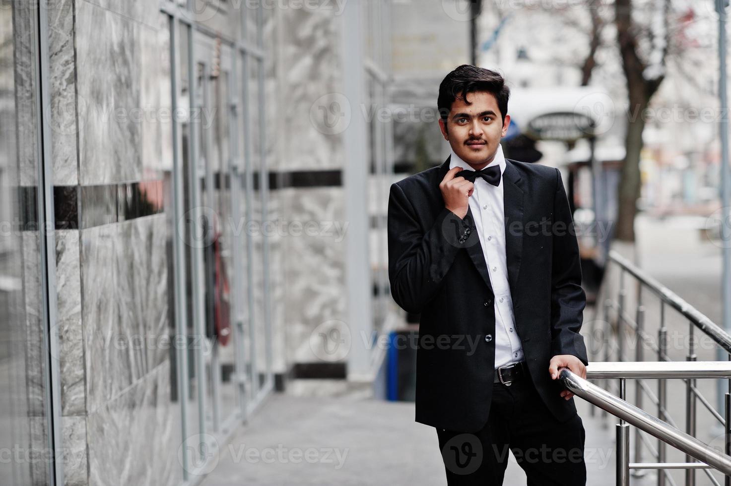 Young indian man on black suit and bow tie posed outdoor. photo