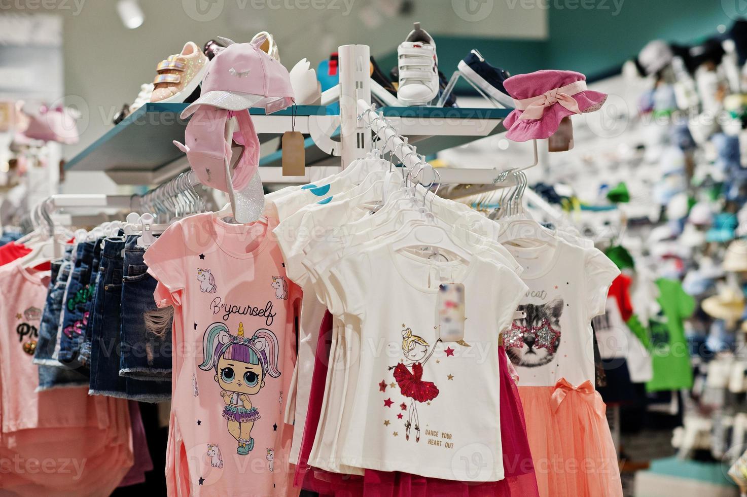 Children's bright clothes hang on the display in the baby clothing store. Girls section. photo