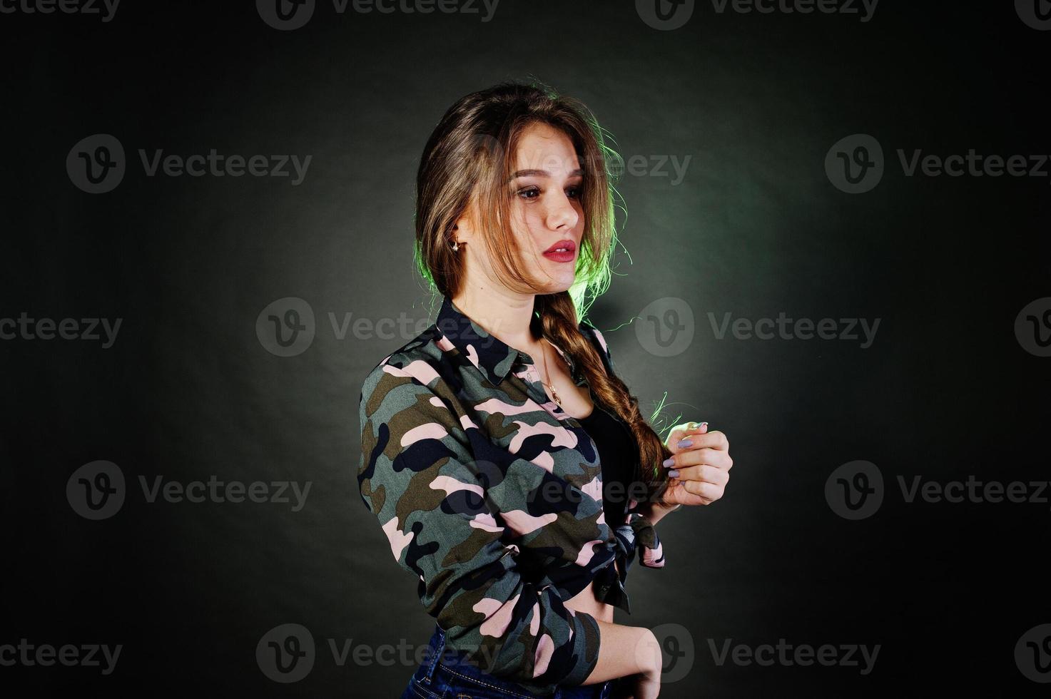 Handsome brunette girl wear military shirt and jeans, posing at studio against gray background. Studio model portrait. photo