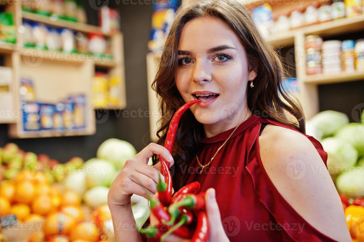 Girl in red holding hot chili peppers on fruits store. photo