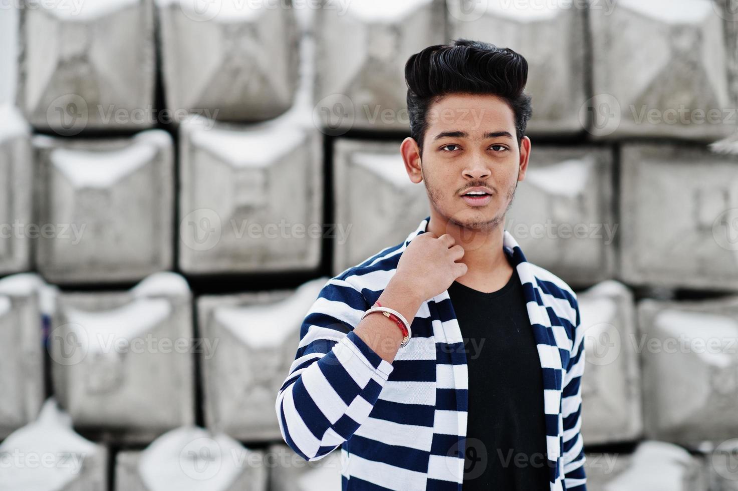 Casual young indian man in stripped sweater posed against stone blocks. photo