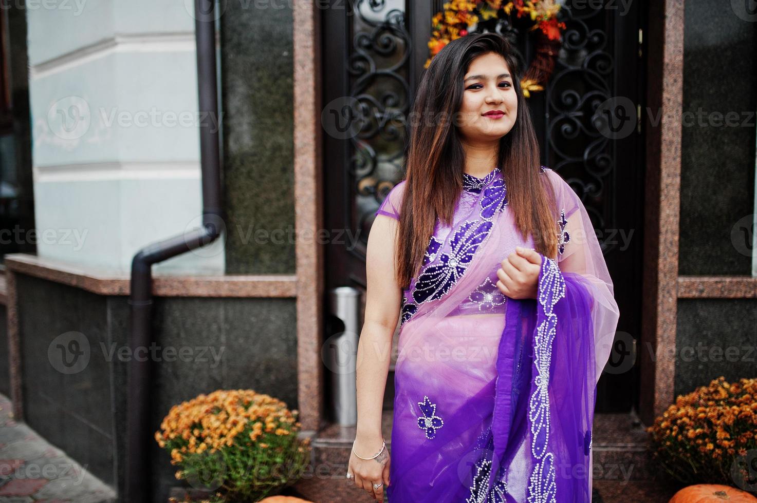Indian hindu girl at traditional violet saree posed at street against door of restaurant with autumn mood and pumpkins. photo