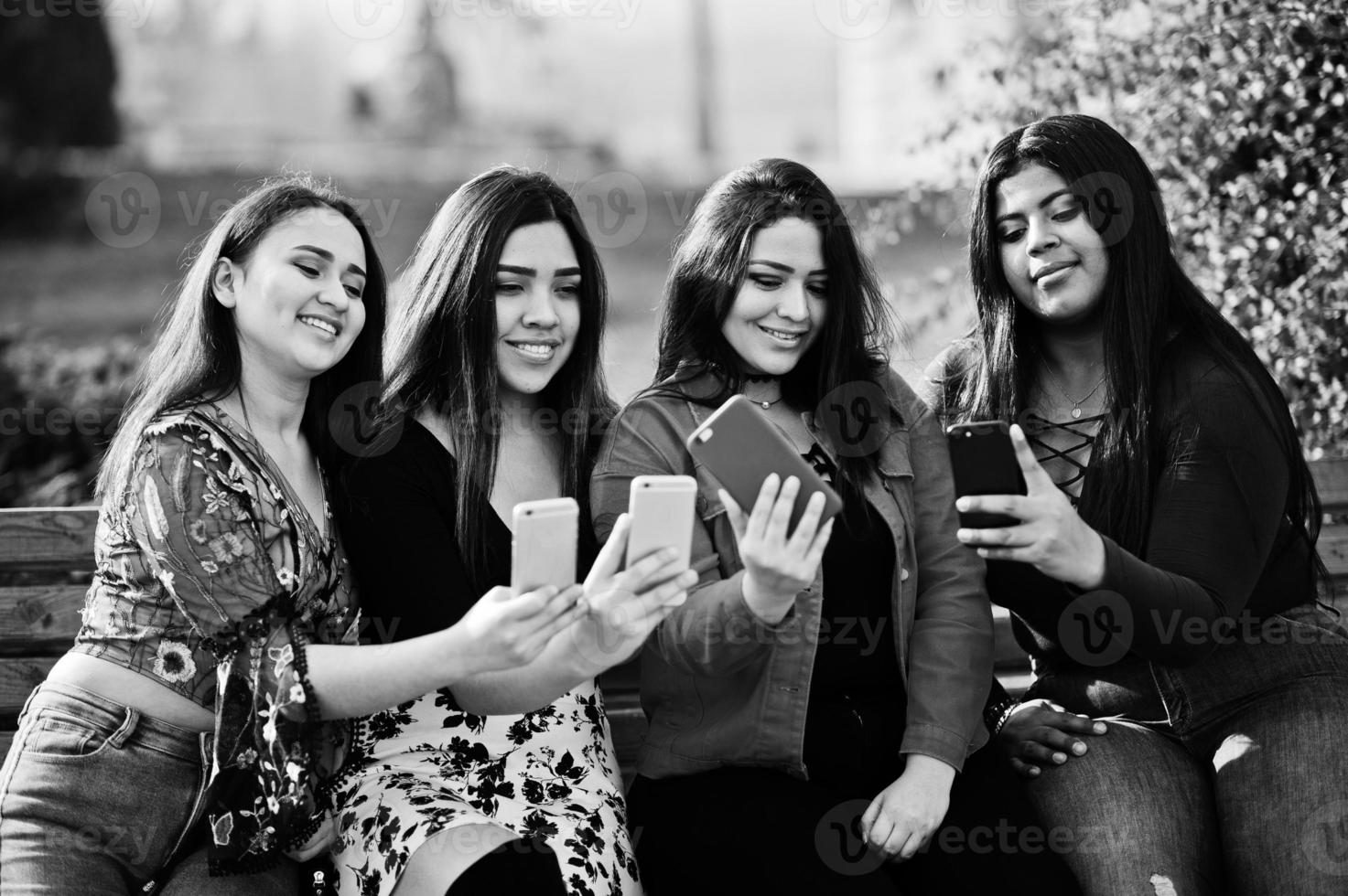 Group of four happy and pretty latino girls from Ecuador posed at street and looking at mobile phones. photo