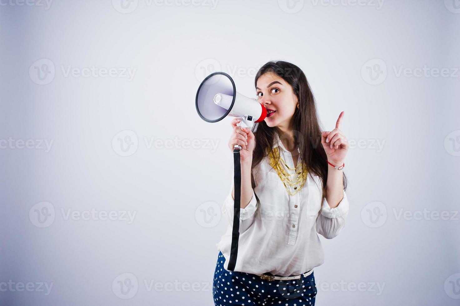 retrato de una mujer joven con pantalones azules y blusa blanca posando con megáfono en el estudio. foto