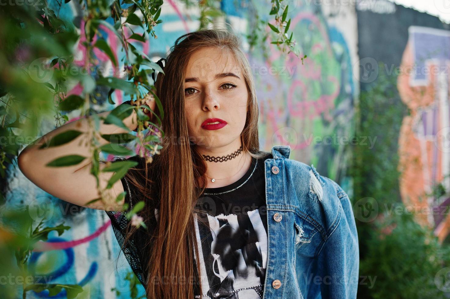 chica hipster casual con estilo en ropa de jeans y gafas contra una gran pared de graffiti. foto