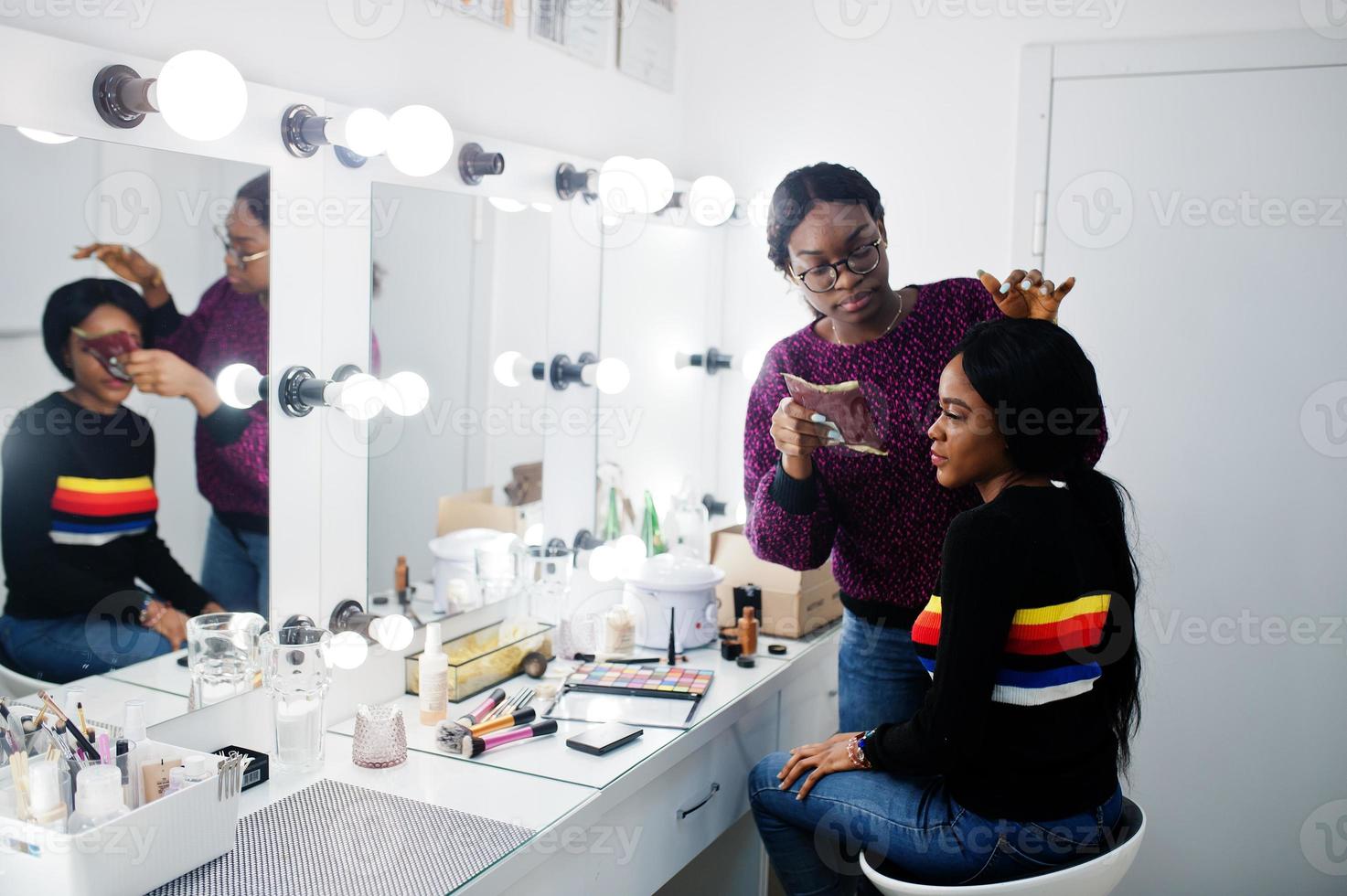 mujer afroamericana aplicando maquillaje por maquillador en el salón de belleza. foto