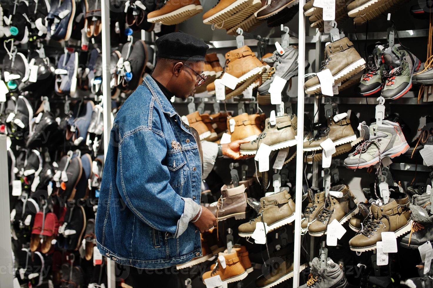 Stylish casual african american man at jeans jacket and black beret at clothes store trying new footwear. photo