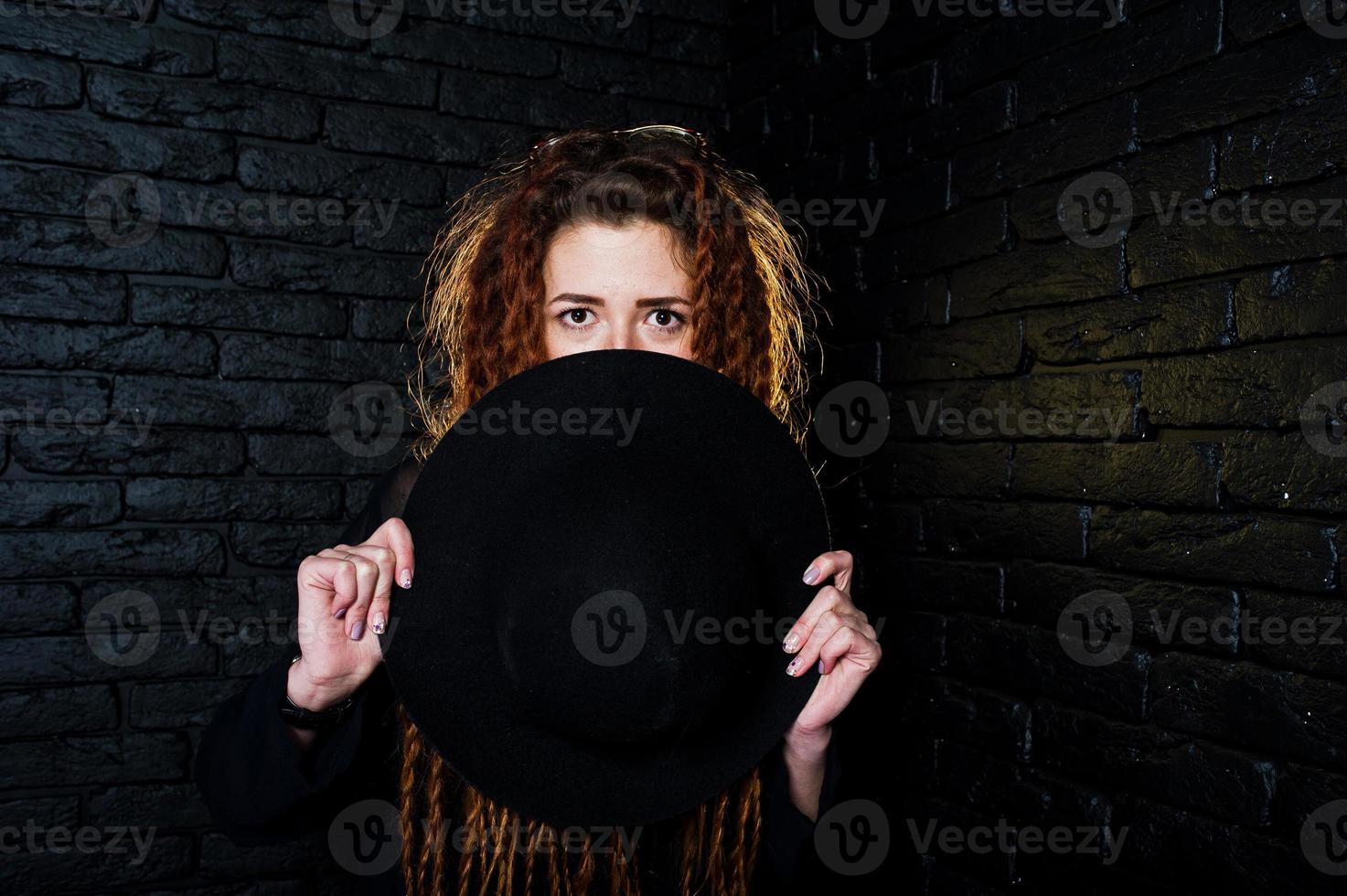 sesión de estudio de una chica de negro con rastas y sombrero sobre fondo de ladrillo. foto
