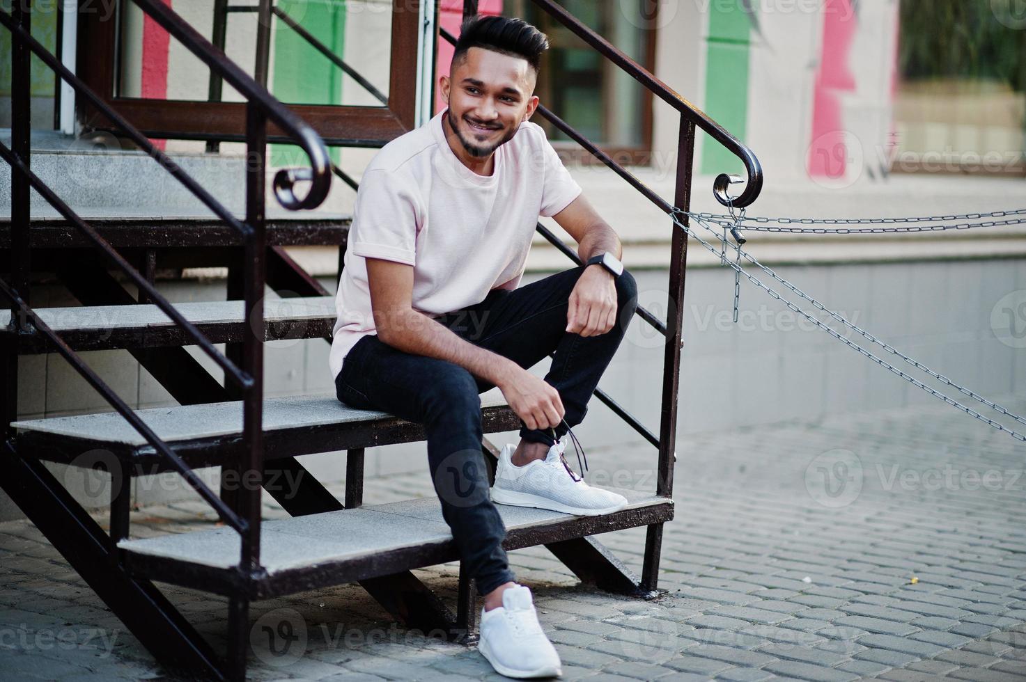 hombre de barba india con estilo en camiseta rosa. modelo india sentada en las escaleras al aire libre en las calles de la ciudad. foto