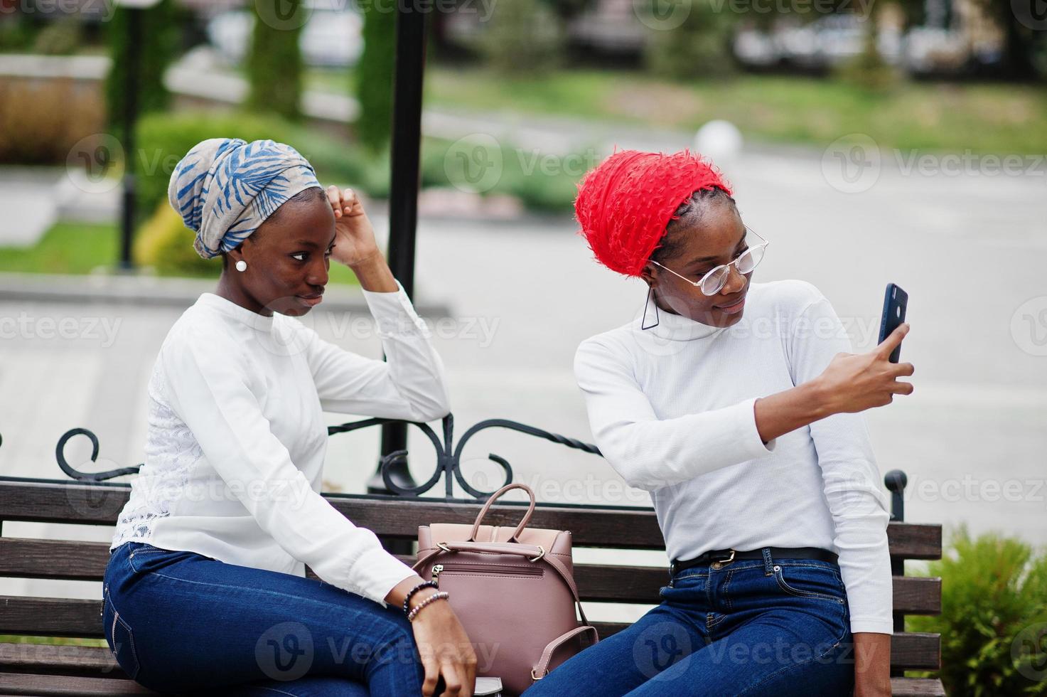 Two young modern fashionable, attractive, tall and slim african muslim womans in hijab or turban head scarf posed together with mobile phones at hands. photo