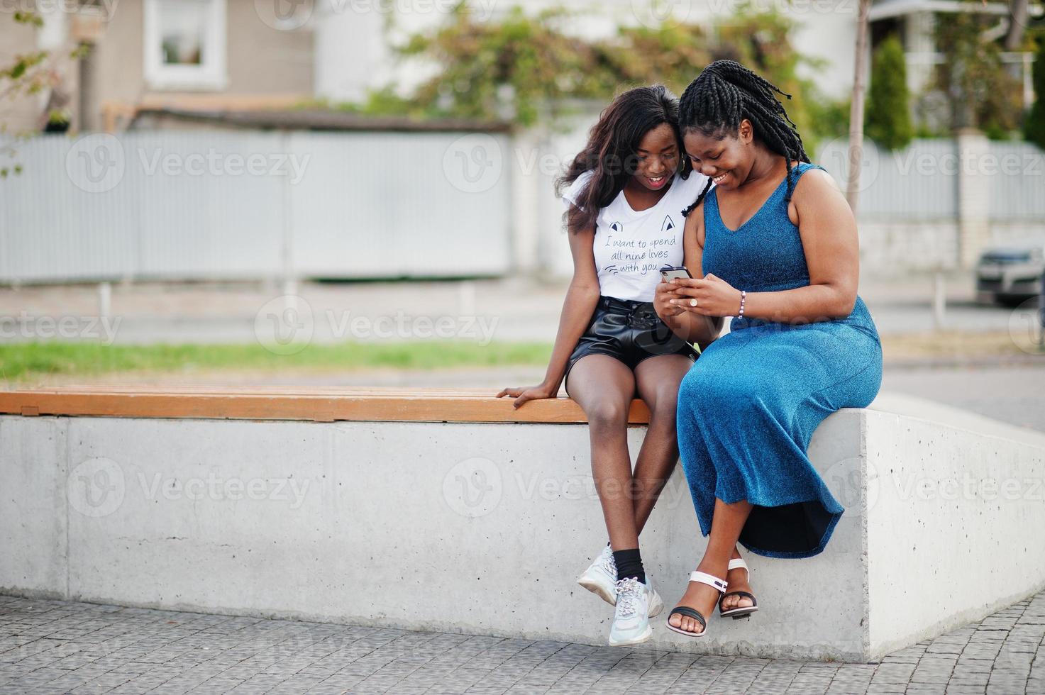 Two african american dark skinned friends female. One of them plus size model, second slim. Having fun and spending time together. Look at mobile phone. photo